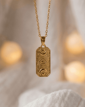 Collana Eyra Giunquilla in oro 18k con carta oracolare, simbolo dell'occhio e fasi lunari Ciondolo Eyra Giunquilla con luna crescente e calante, gioiello di protezione e conoscenza Collana pendente Giunquilla con simboli oracolari in acciaio dorato, energia di visione interiore Ciondolo Giunquilla con occhio e luna, amuleto del sacro femminile in oro 18k su mussola chiara Collana Eyra Giunquilla: occhio apotropaico e fasi lunari in acciaio placcato oro 18k