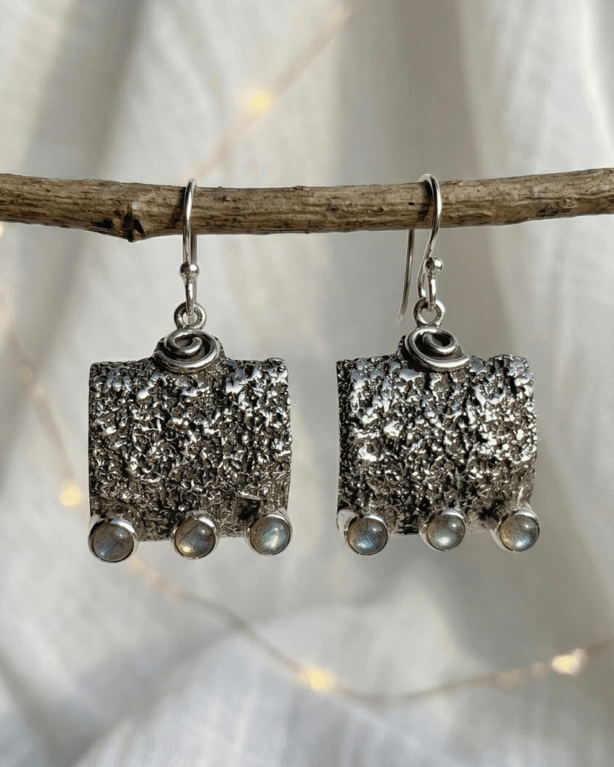 Orecchini pendenti Wayra Giunquilla in argento 925 con labradorite, equilibrio tra terra e luna Orecchini Giunquilla con labradorite cangiante in argento 925, radicamento e flusso ciclico femminile Orecchini quadrati pendenti Giunquilla in argento con labradorite e spirale, simboli del cosmo Orecchini Wayra Giunquilla argento 925 e labradorite: energia terrestre e ritmo interiore al lobo Orecchini pendenti Giunquilla con labradorite in argento 925, gioiello spirituale del sacro femminile