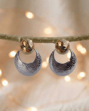 Orecchini Marisol Giunquilla in oro 18k con sole e luna a finitura martellata Orecchini pendenti Giunquilla con sole e luna dorati, simbolo di dualità e visione interiore Orecchini Giunquilla con sole e luna in acciaio placcato oro 18k, energia solare e lunare al lobo Orecchini Marisol Giunquilla, finitura martellata dorata: la danza degli opposti come gioiello Orecchini pendenti Giunquilla con simboli solari e lunari, protezione e connessione con i cicli naturali